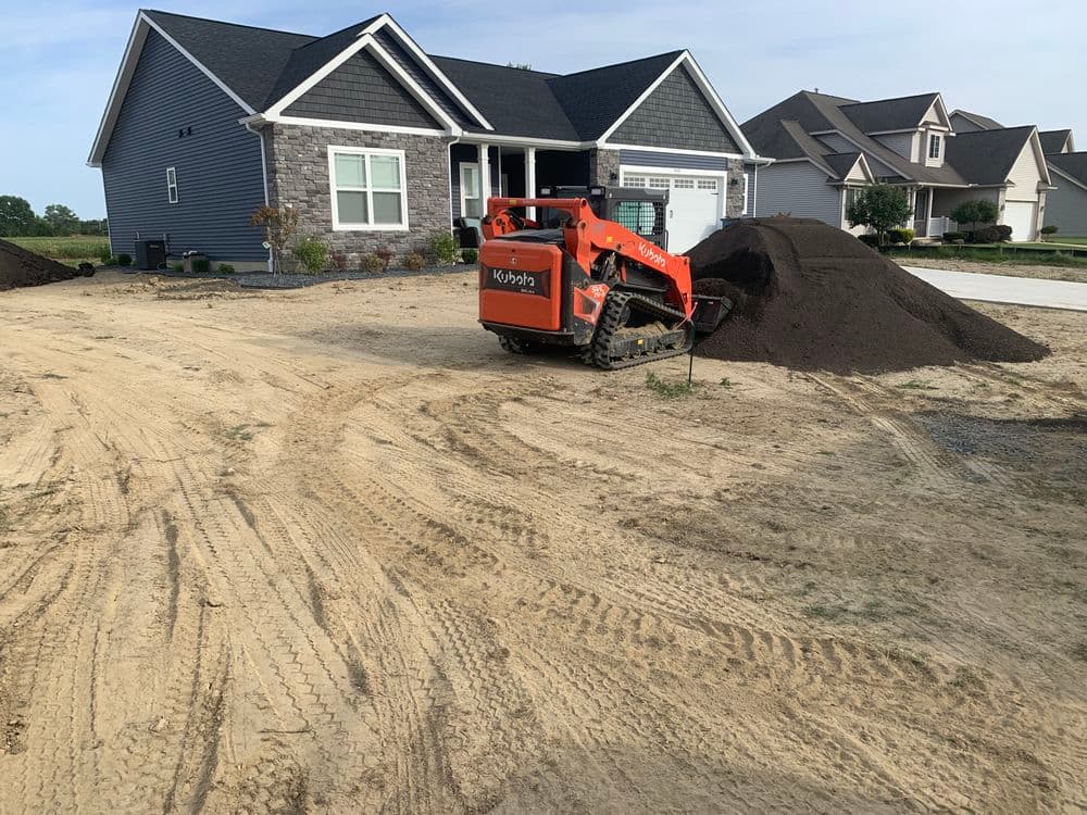 Bobcat moving soil near a new home construction site with dirt pile in foreground.