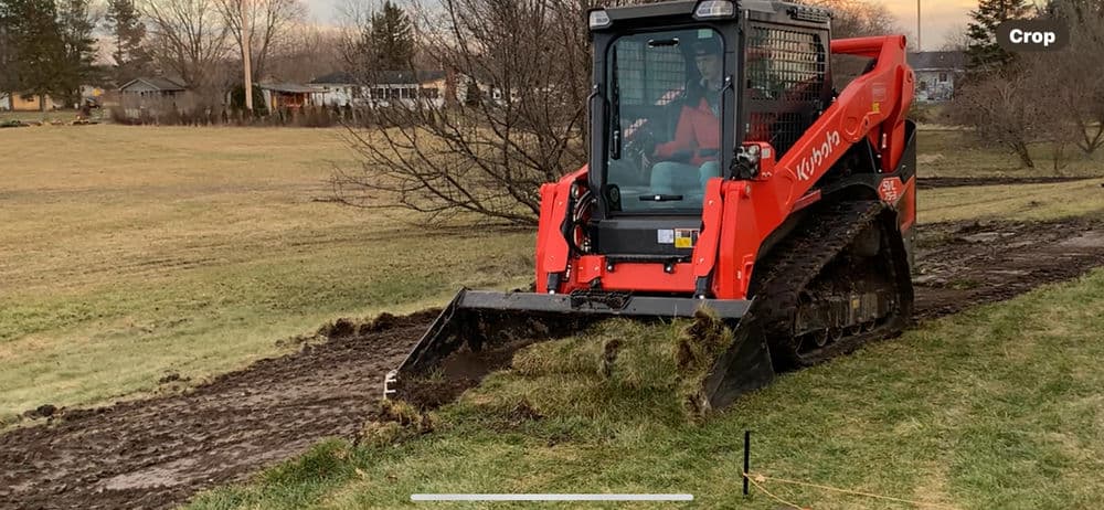 Kubota skid steer loader leveling terrain in a grassy field during sunset.